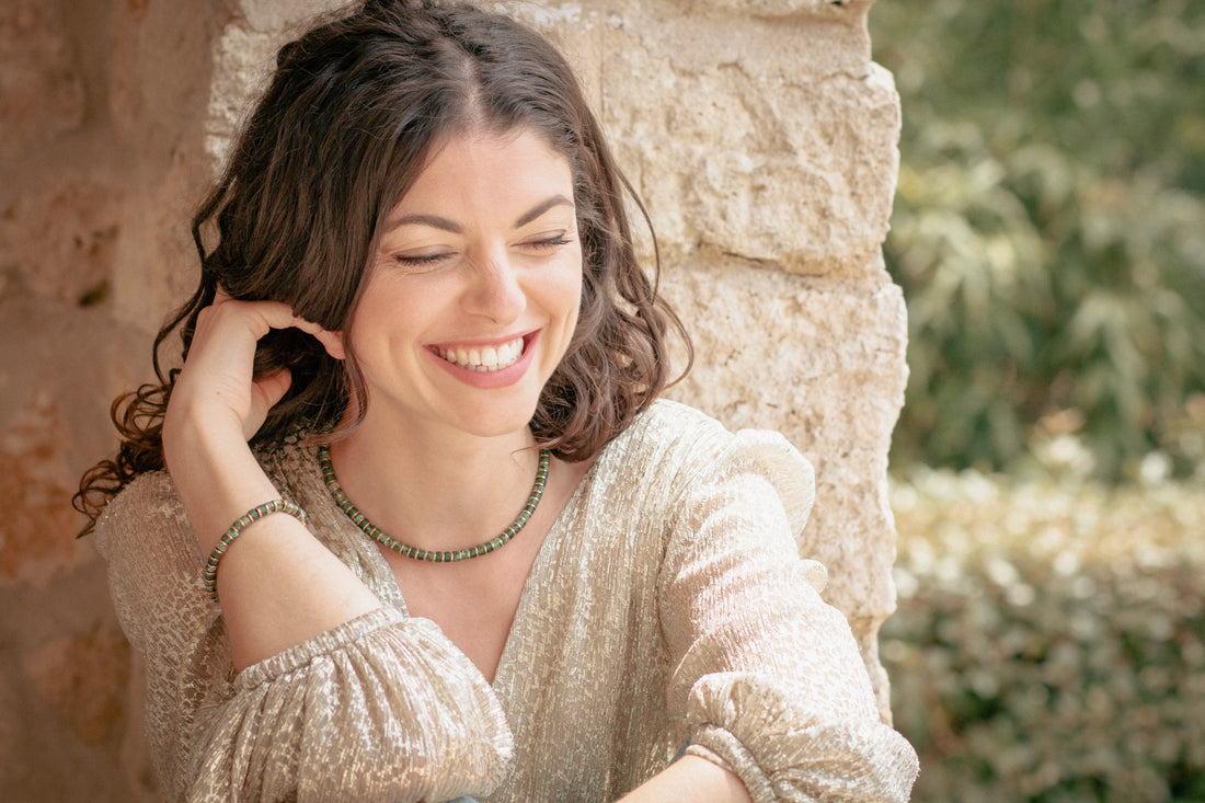 Femme souriante en robe de soirée invitée à un mariage portant un bracelet et un collier en perles vert et or