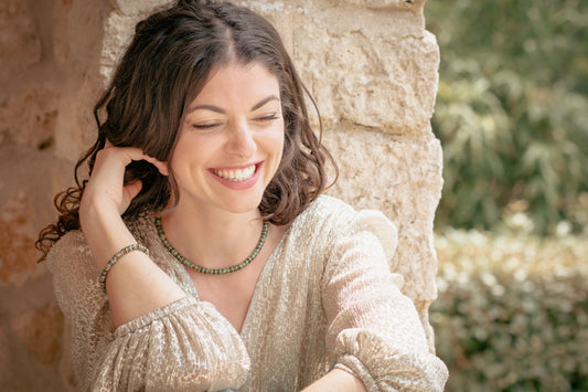Femme souriante en robe de soirée invitée à un mariage portant un bracelet et un collier en perles vert et or