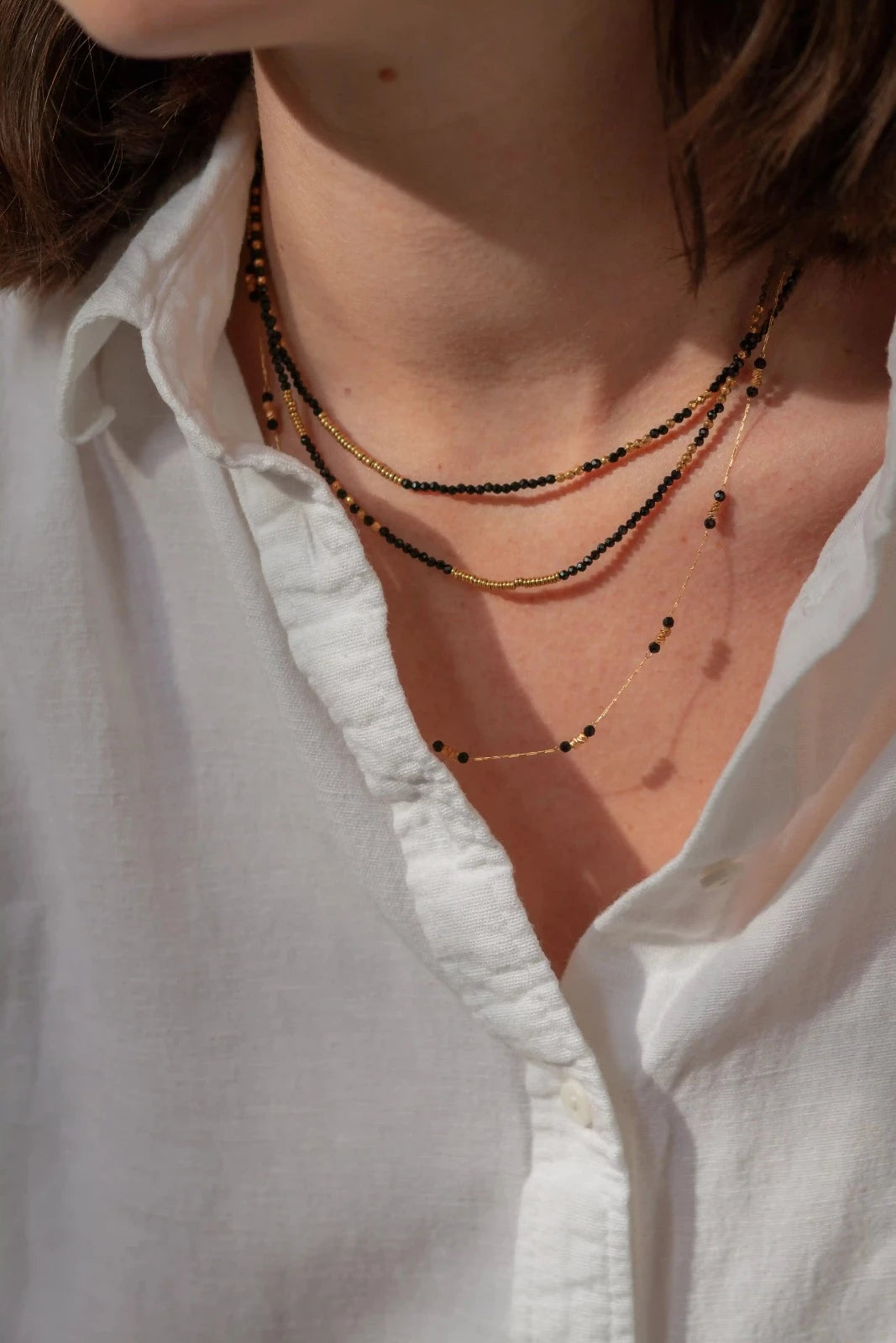 femme portant trois colliers de perles noir et or fins et élégants