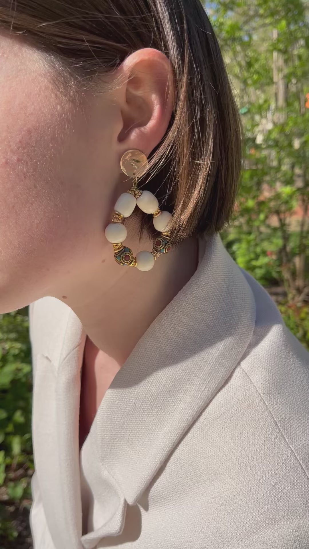 Femme aux cheveux châtains portant des grosses boucles d'oreilles or et crème perles tibétaines et en résine beige ethniques