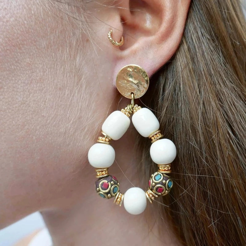 Femme aux cheveux châtains portant des grosses boucles d'oreilles or et crème perles tibétaines et en résine beige ethniques