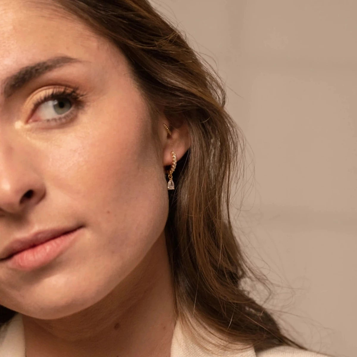 Femme brune portant de fines et élégantes boucles d'oreilles dorées, avec un strass au bout