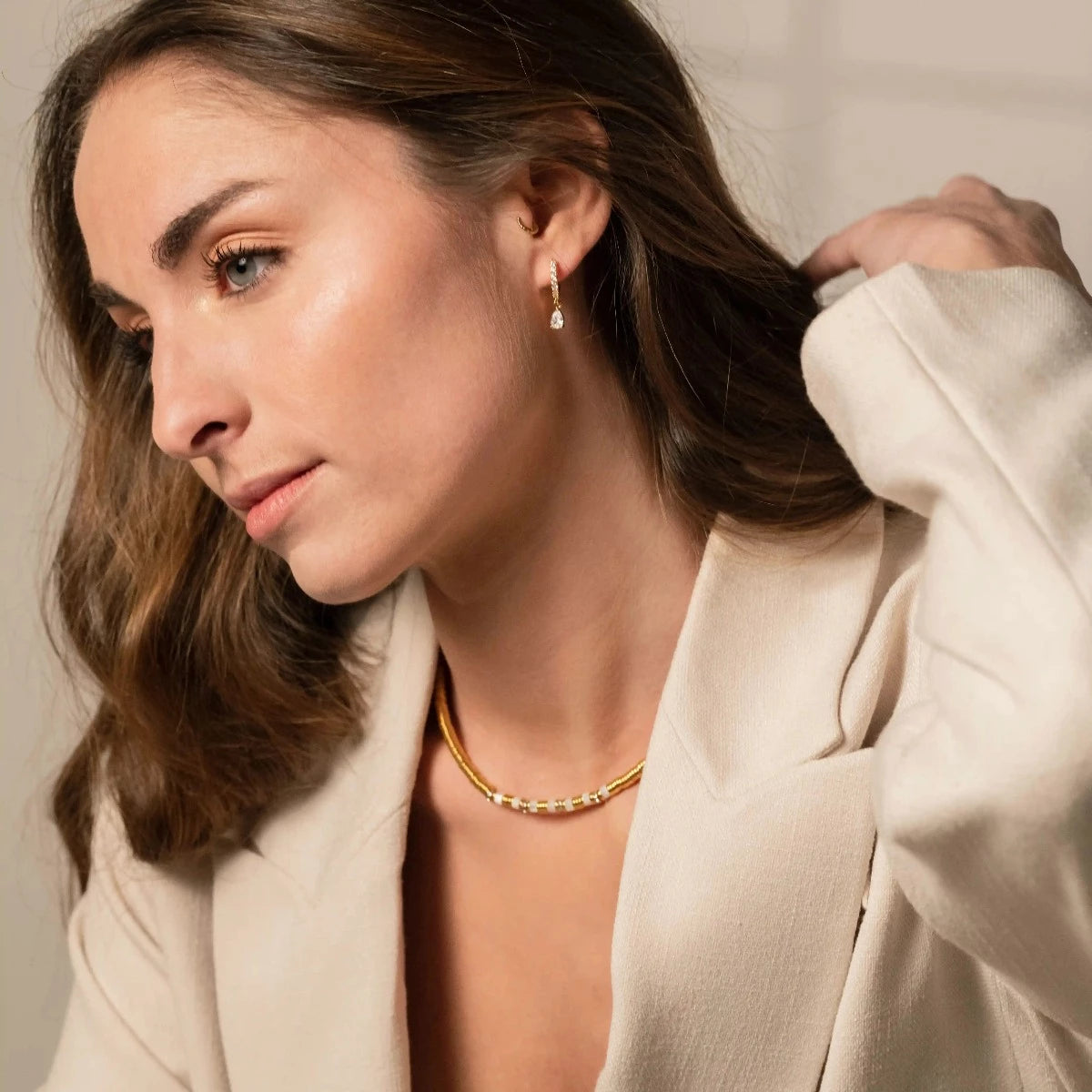 Femme brune portant de fines et élégantes boucles d'oreilles dorées, avec un strass au bout