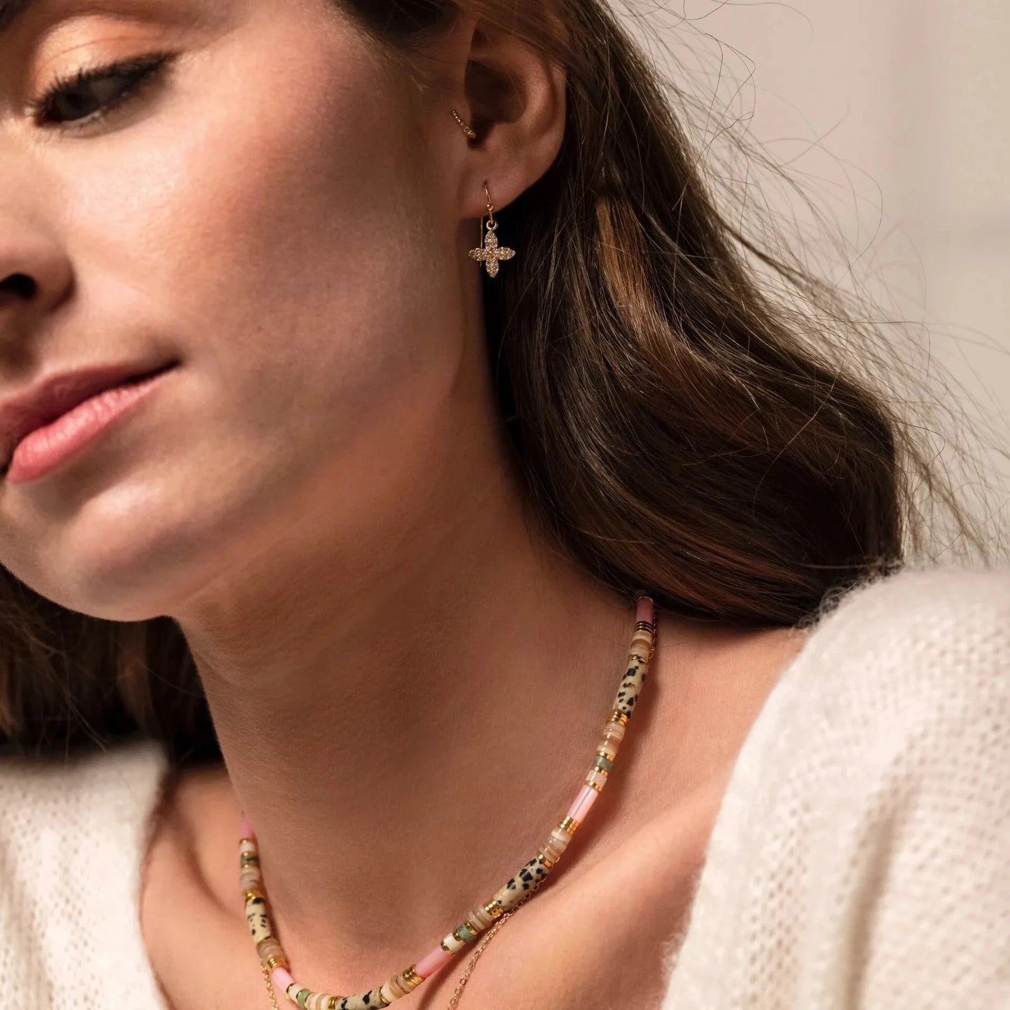 Femme brune portant des boucles d'oreilles or et strass en forme de croix