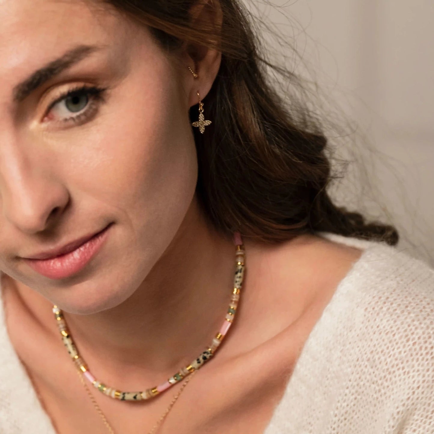 Femme brune portant des boucles d'oreilles or et strass en forme de croix