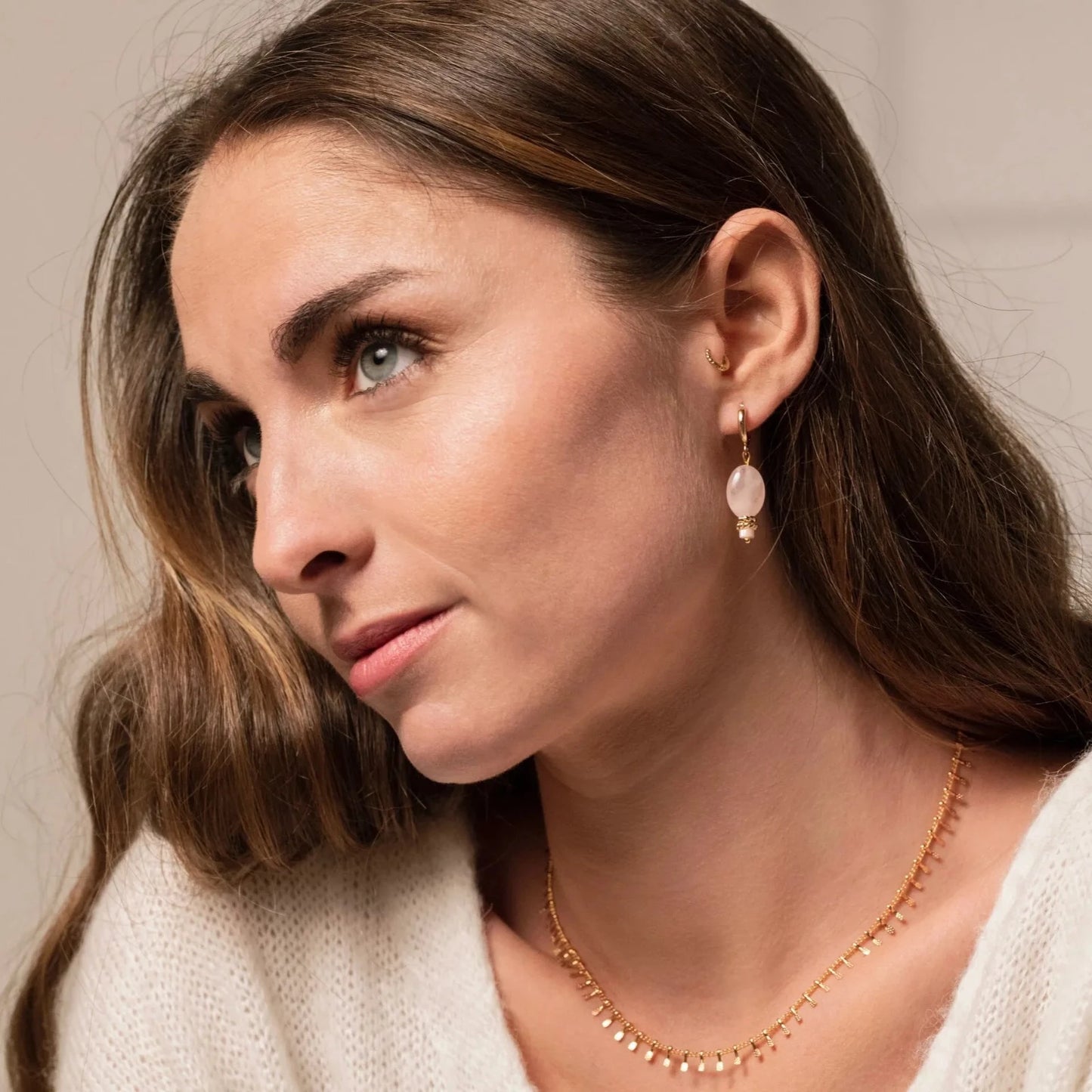 Femme brune portant de fines boucles d'oreilles en or et pierre rose ainsi qu'un collier chaine en or