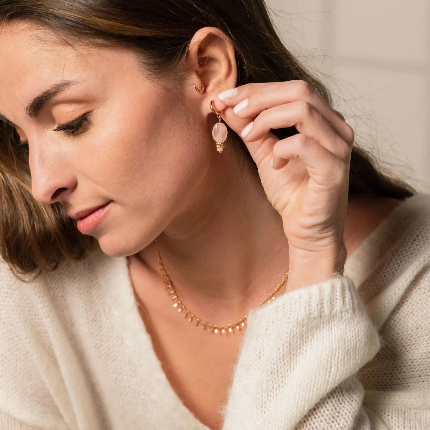 Femme brune portant de fines boucles d'oreilles en or et pierre rose ainsi qu'un collier chaine en or