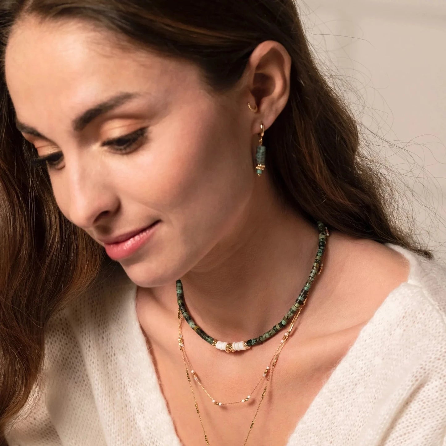 Jolie jeune femme portant des bijoux en accumulation : colliers de perles, chaines de cou, boucles d'oreilles en pierres naturelles