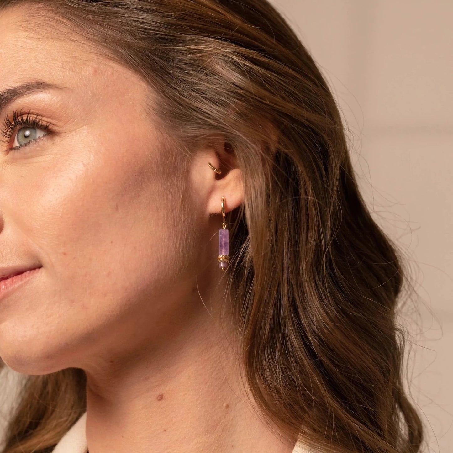 Jeune femme brune portant des boucles d'oreilles de soirée en or et pierre naturelle violette