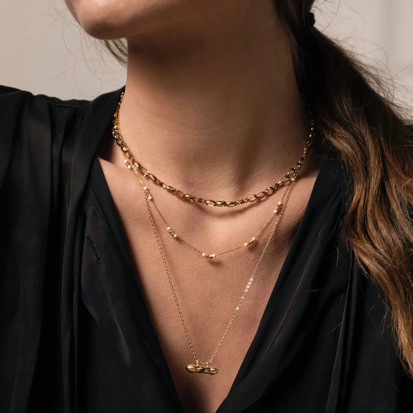 Femme au chemisier noir portant une accumulation de trois colliers de différentes longueurs en perles et chaine plaqué or