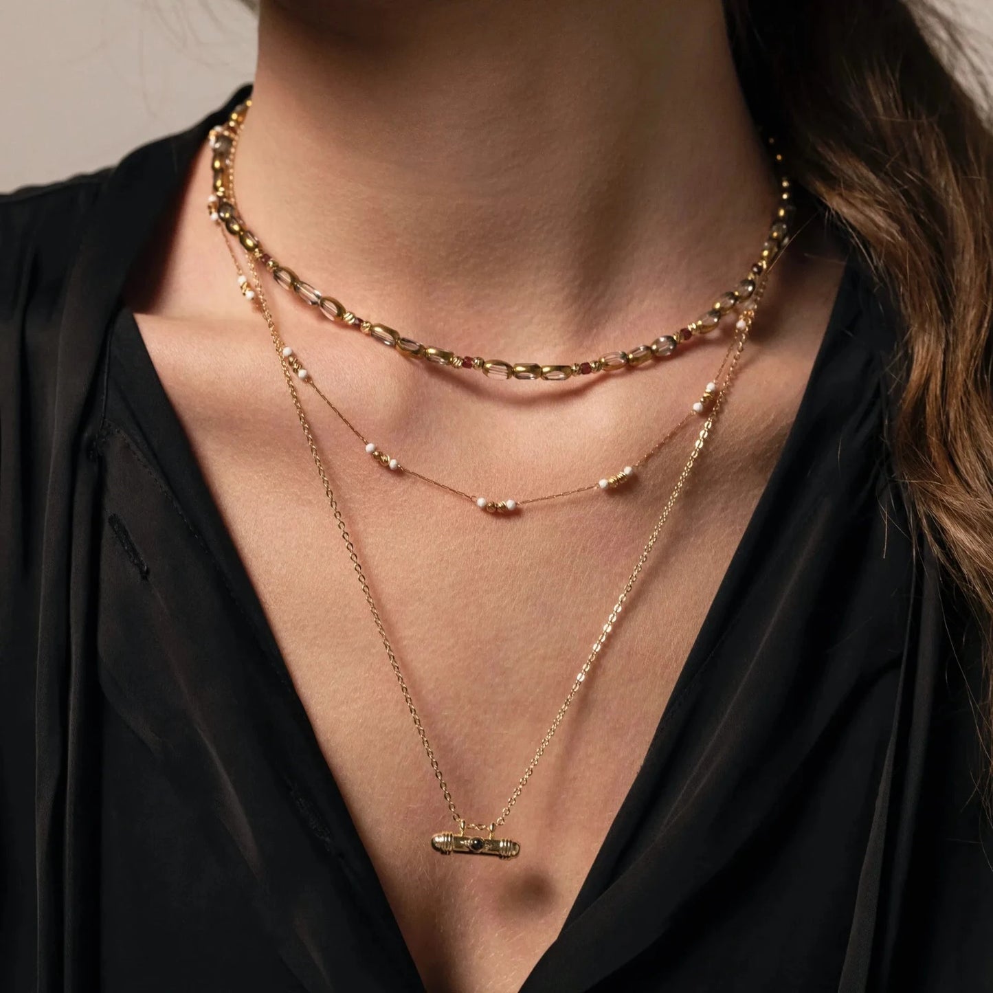 Femme au chemisier noir portant une accumulation de trois colliers de différentes longueurs en perles et chaine plaqué or