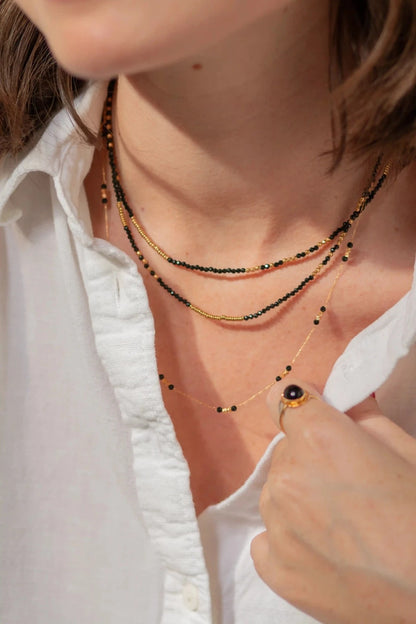 femme portant trois colliers de perles noir et or fins et élégants