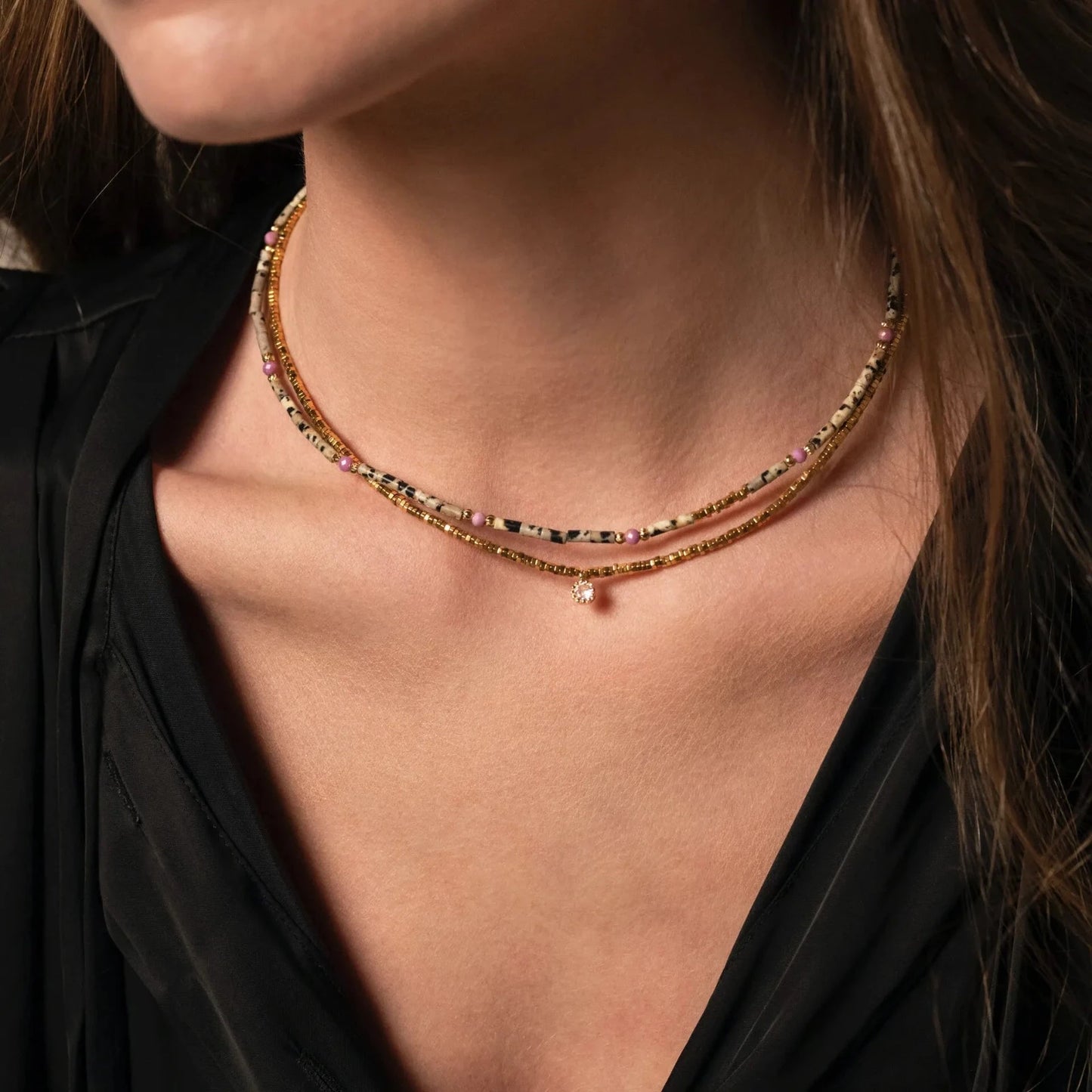 Femme au chemisier noir portant des colliers en pierres et perles fines et plaqué or 