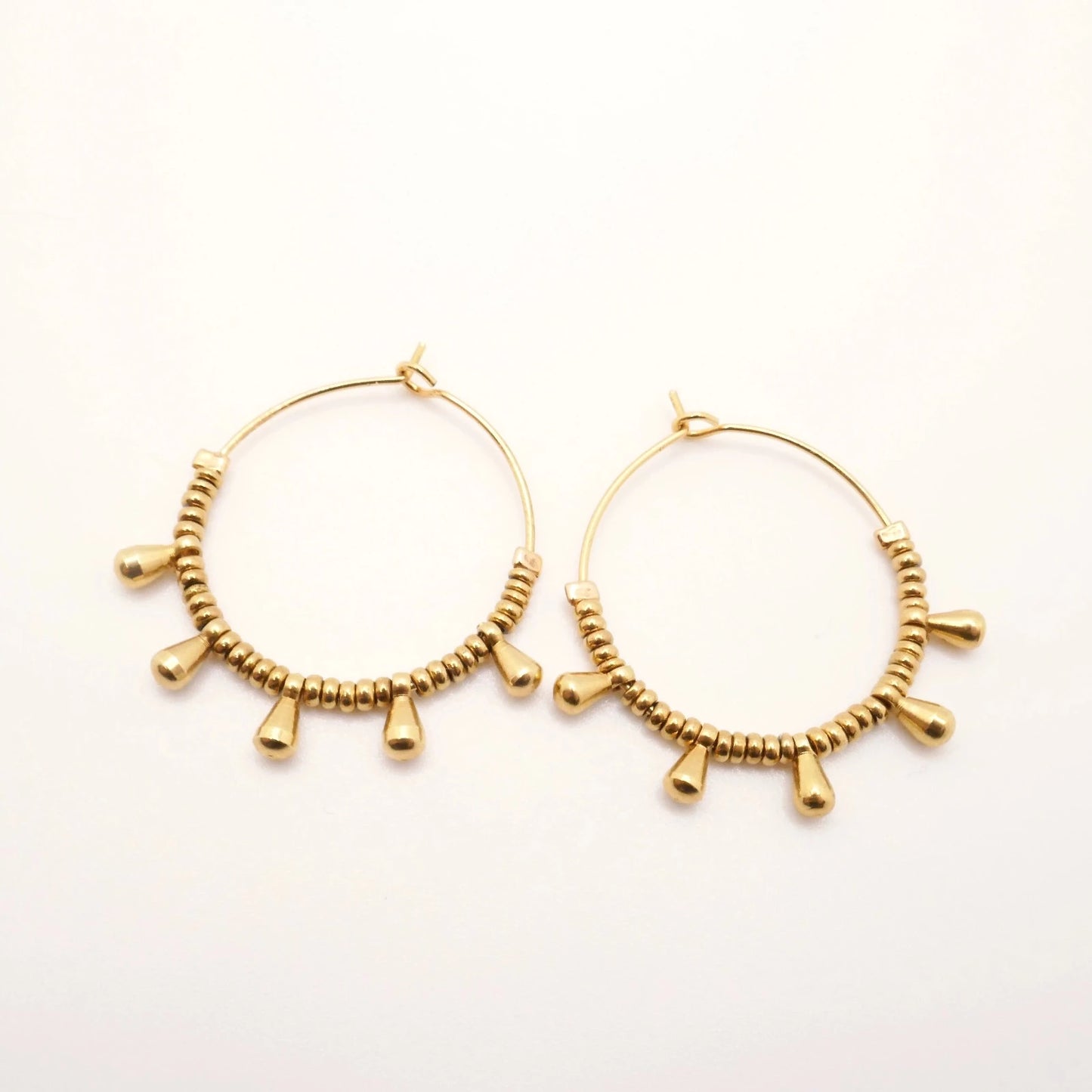 Boucles d'oreilles créoles pour femme en mini perles d'Hématite dorées à l'or fin sur fond blanc