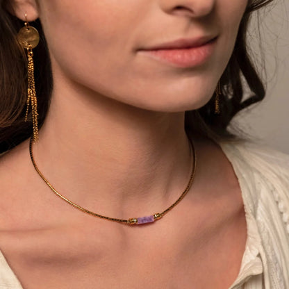 Femme brune portant des boucles d'oreilles dorées pendantes et un collier doré et violet