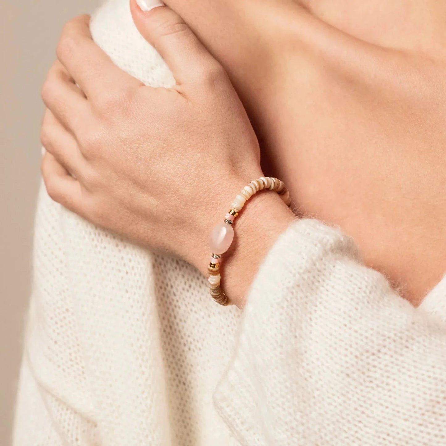 Femme portant au poignet un bracelet en perles beiges et dorées et pierre semi-précieuse de Quartz rose