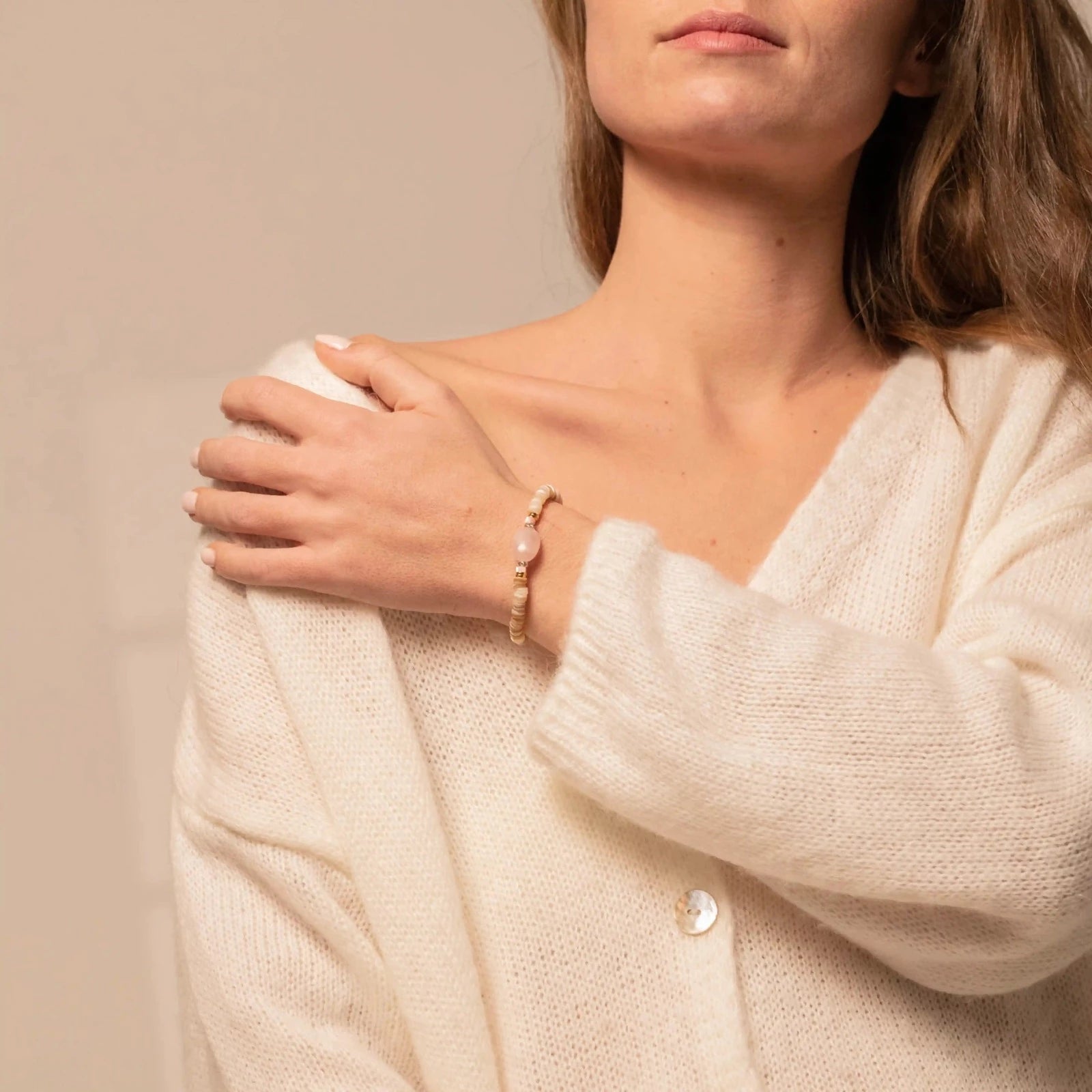 Femme portant au poignet un bracelet en perles beiges et dorées et pierre semi-précieuse de Quartz rose