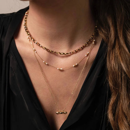 femme au chemisier noir portant deux colliers en perles et une chaine dorée avec médaillon