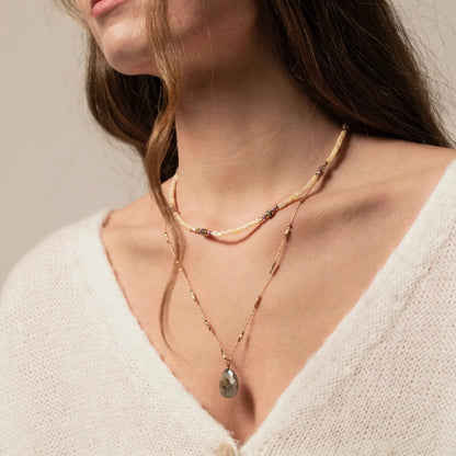Femme portant deux colliers : un en perles de coquillages jaune poudré, l'autre un sautoir avec médaillon en pierre