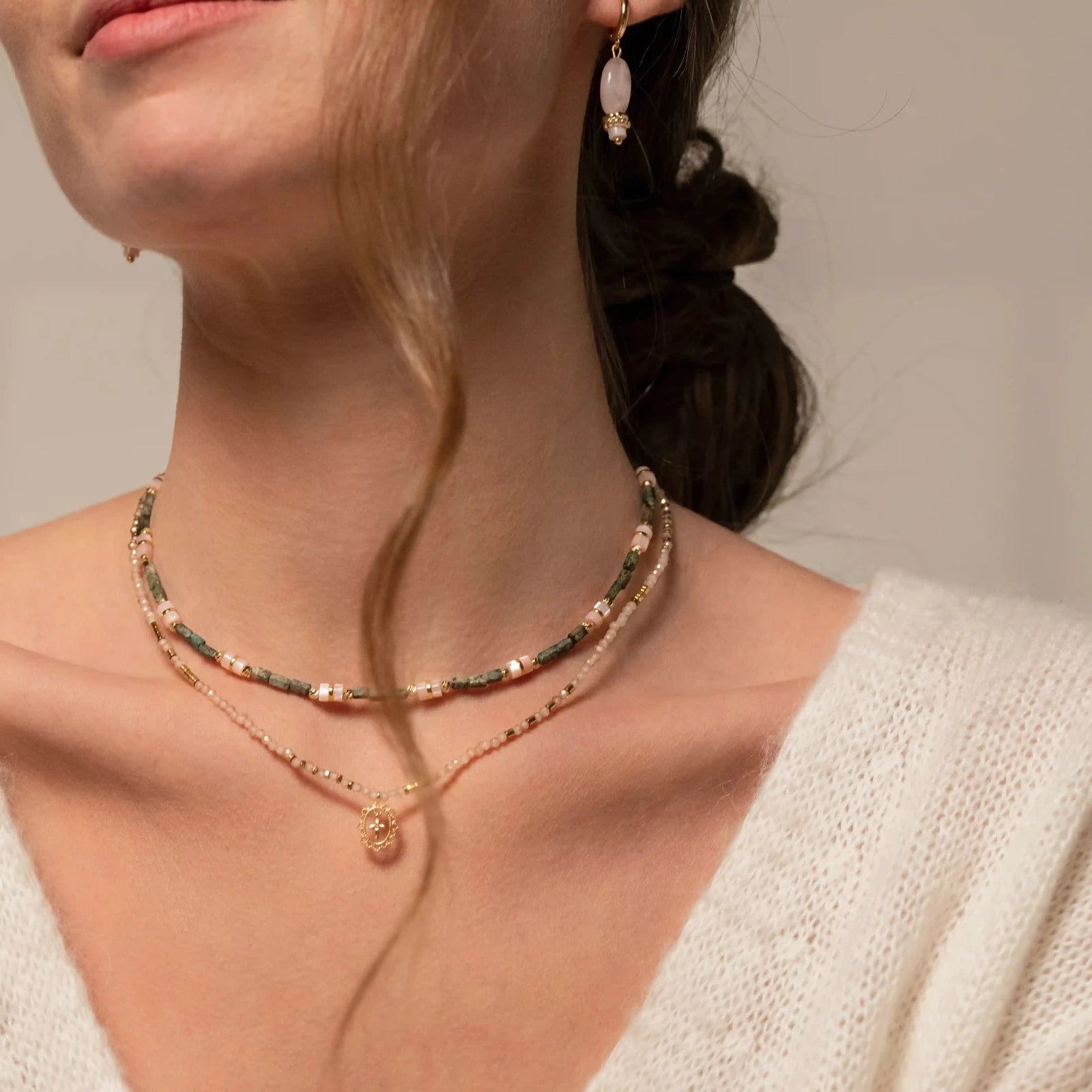 femme portant des colliers en perles dont un avec un pendentif doré en forme de croix