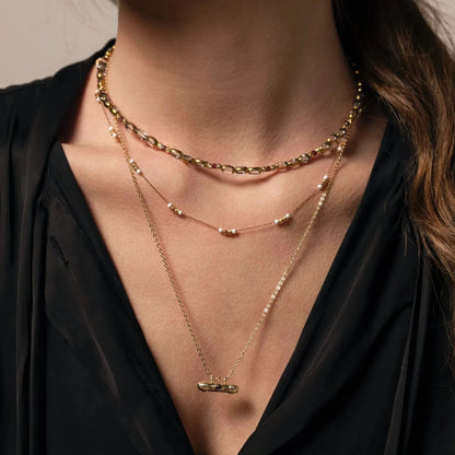 Femme au chemisier noir portant une accumulation de trois colliers de différentes longueurs en perles et chaine plaqué or 