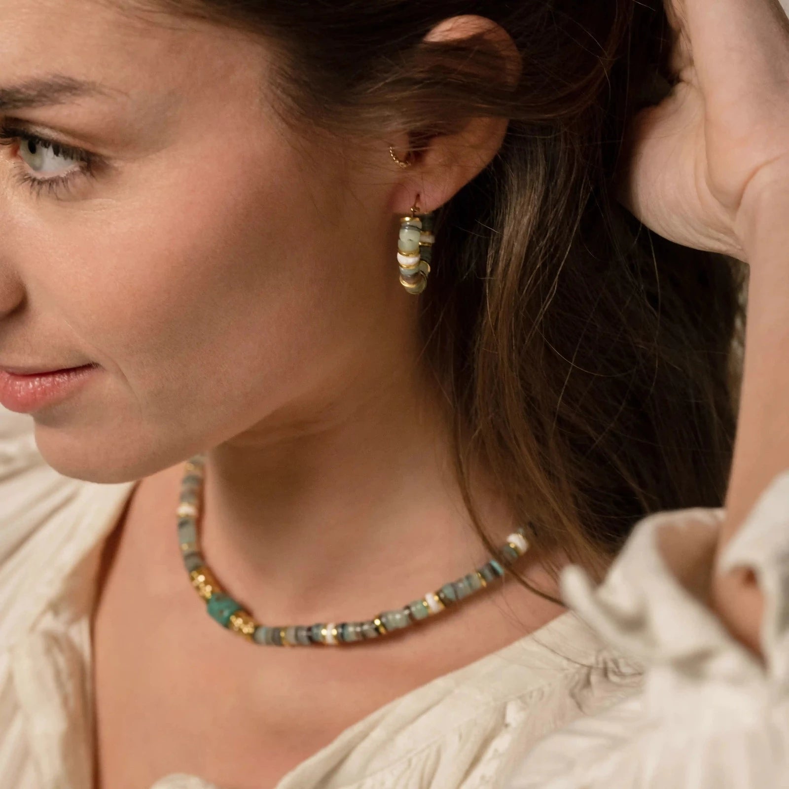 Femme portant des boucles d'oreilles créoles et un collier en perles vertes