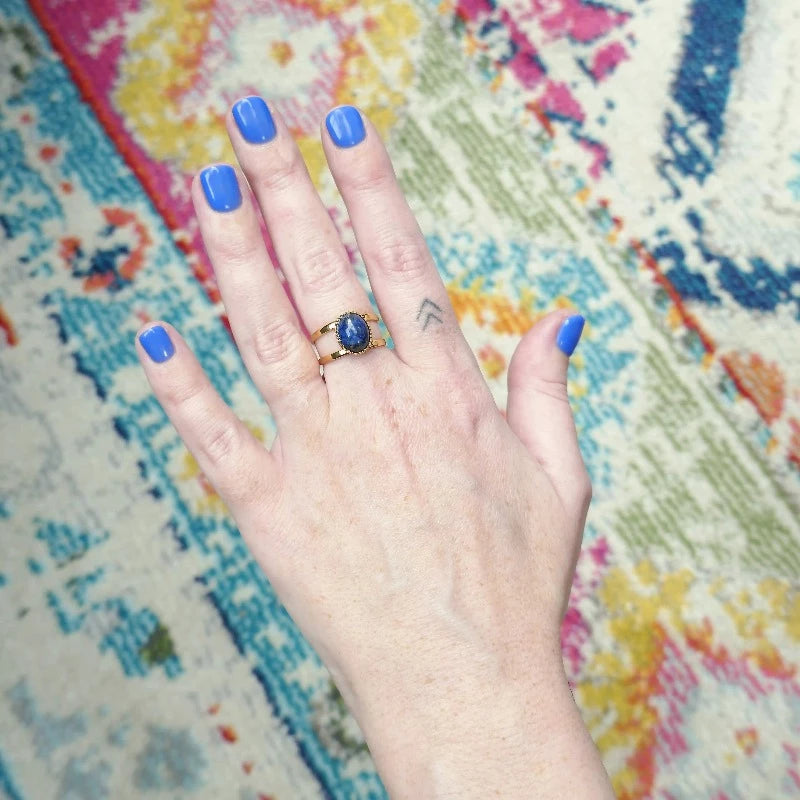 main de femme au venis bleu portant une bague en or et sa pierre semi-précieuse bleue