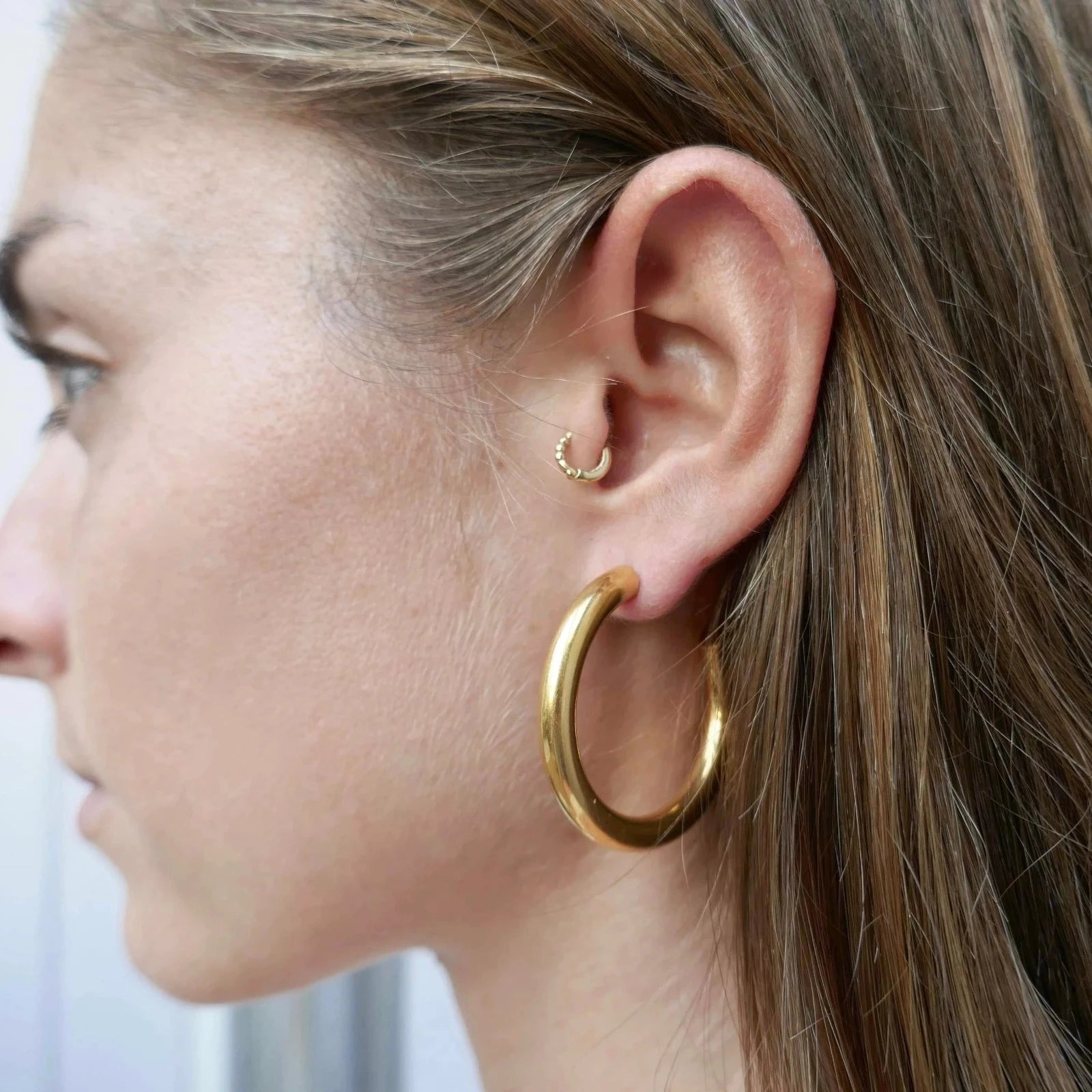 Femme cheveux châtains portant des créoles dorées élégantes et légères